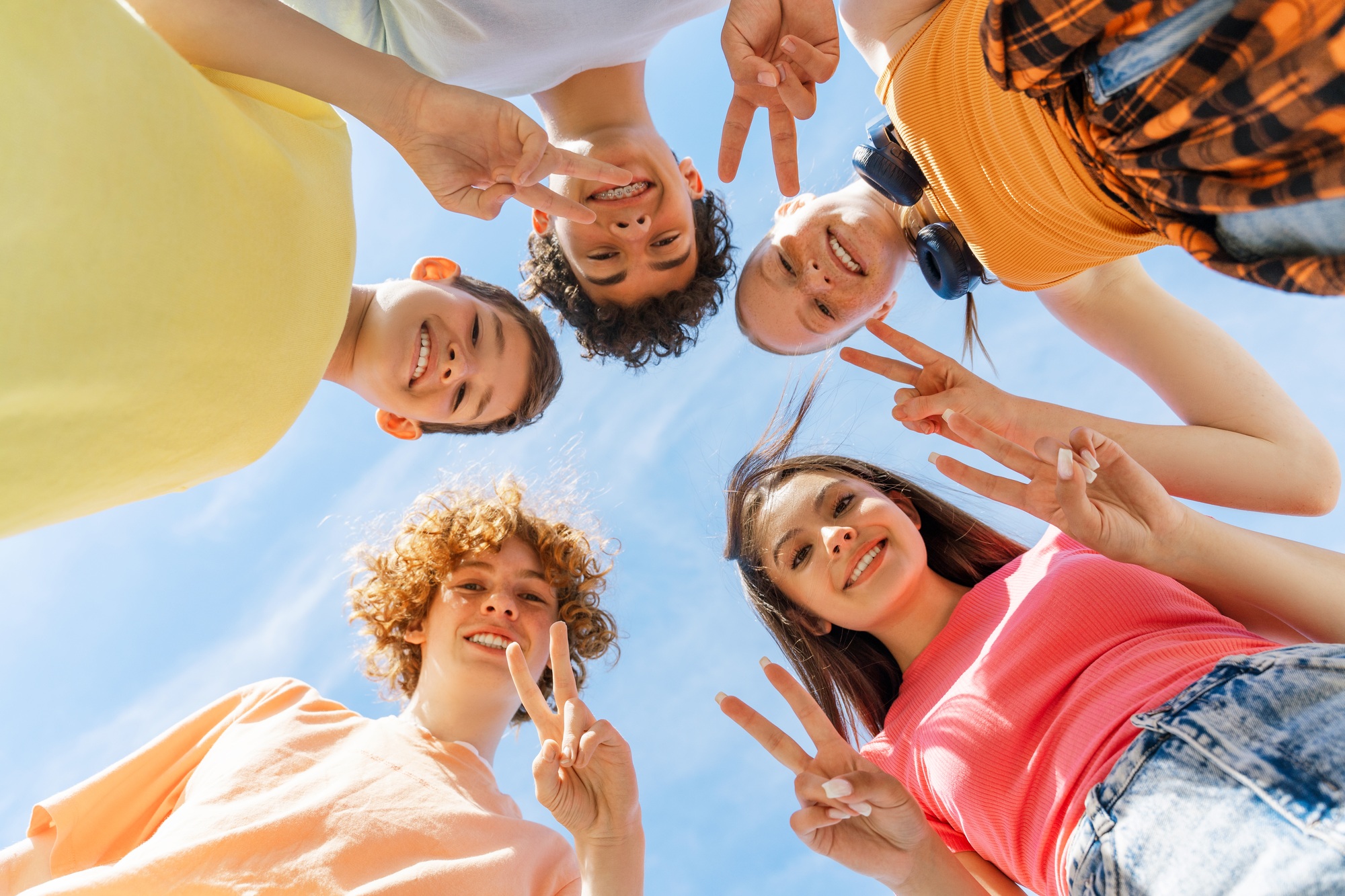 Happy children showing peace hand sign and standing in circle, looking at camera