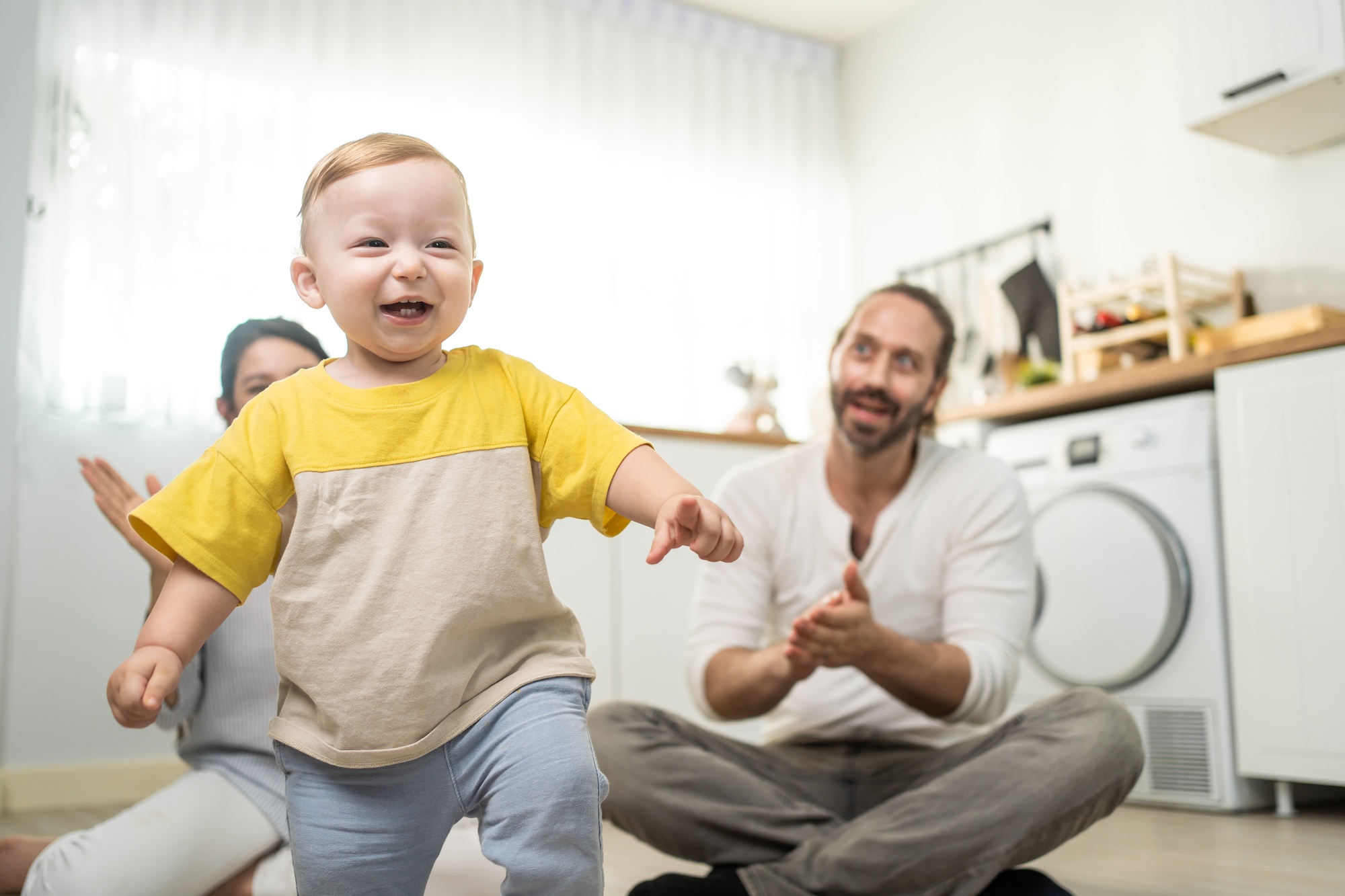 Caucasian baby boy child learn to walk with parents support in house.