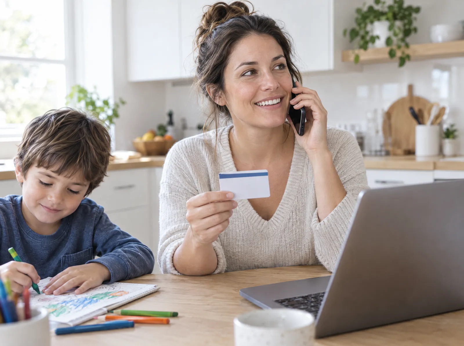 A mother holds an insurance card and smiles during a phone call at her kitchen table